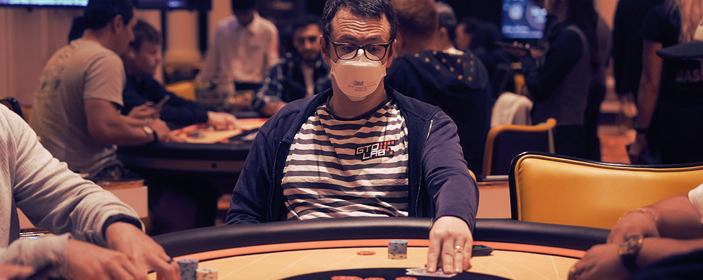 Isaac “Ike” Haxton focused at a Triton Poker final table, wearing his signature N95 mask and hoodie under studio lights during the 2025 Jeju II PLO Main Event.