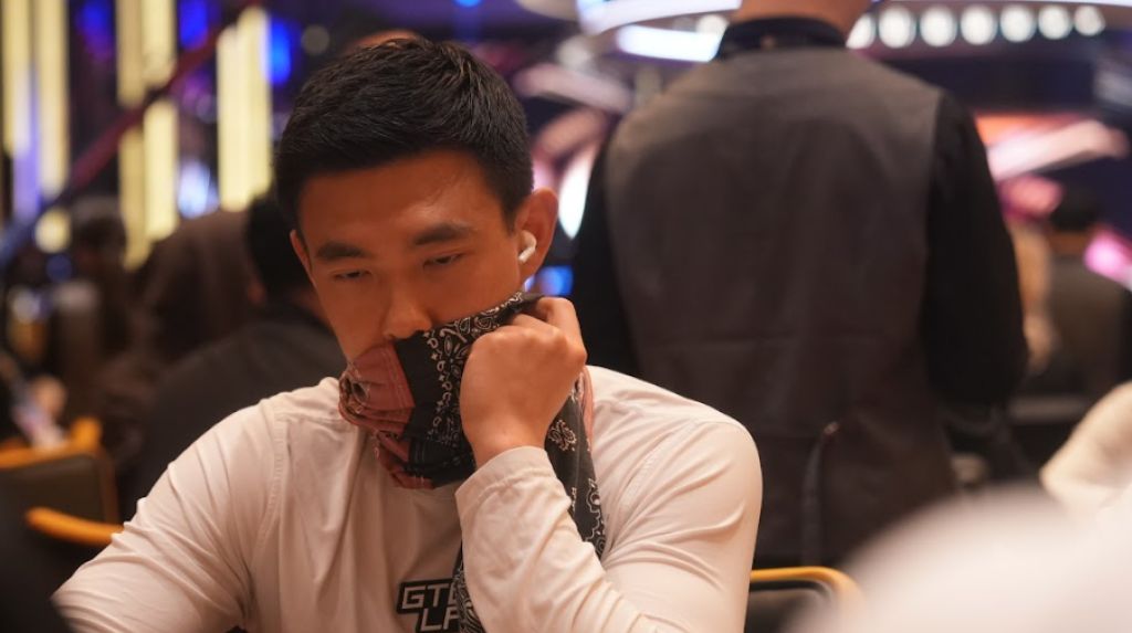 GTO LAB coach Brian Kim playing live poker at a tournament, holding a bandana up to his face and looking down at the table.
