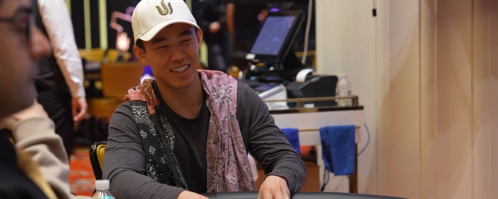 Professional poker player Brian Kim smiling at the table wearing a white cap during a live event.