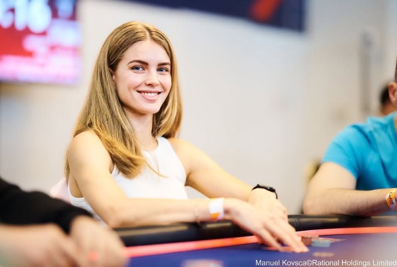 Diana Kalietina seated at a poker table, smiling and focused before play.